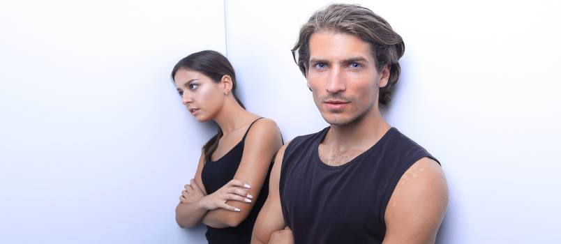 Young sad couple standing near white wall