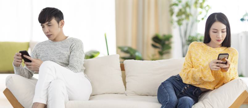 Young couple sitting on sofa using their smartphones