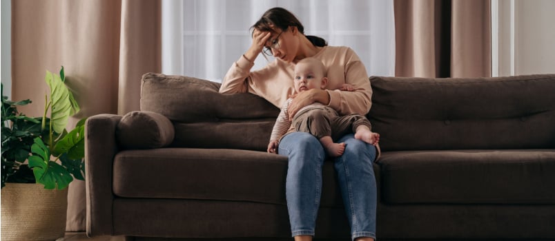 Depressed mother sitting on couch holding kid