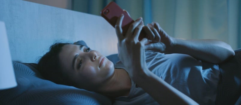 Woman laying on bed using smartphone