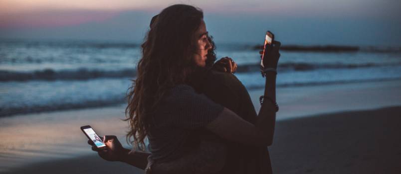 Couple hugging while using smartphone