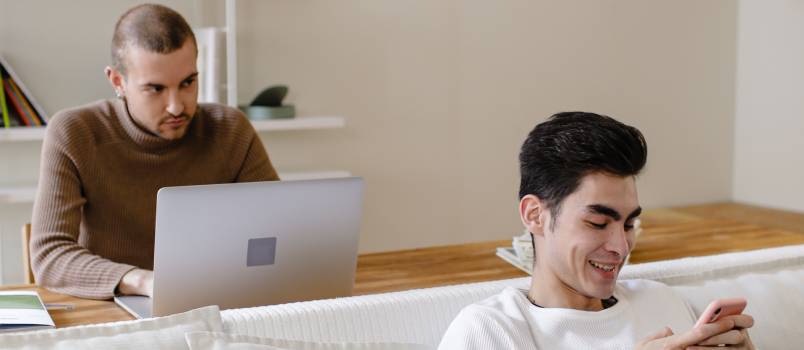 Man working on laptop while other man is using mobile phone