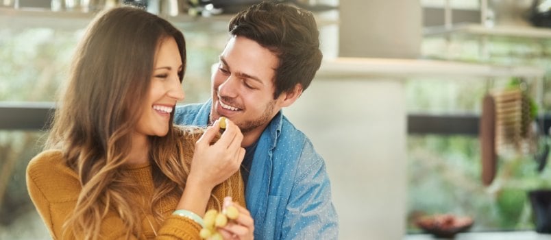Woman feeding grapes to man in kitchen