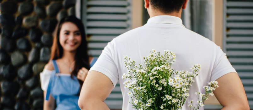 Man holding flowers for woman standing infront