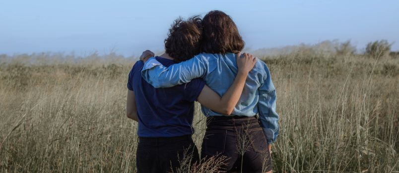Female friend embracing on specious meadow