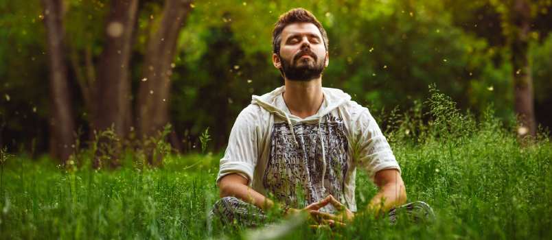 Man meditating sitting on green grass