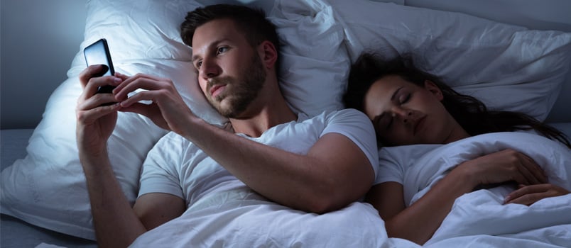 Young woman using cellphone while wife is asleep