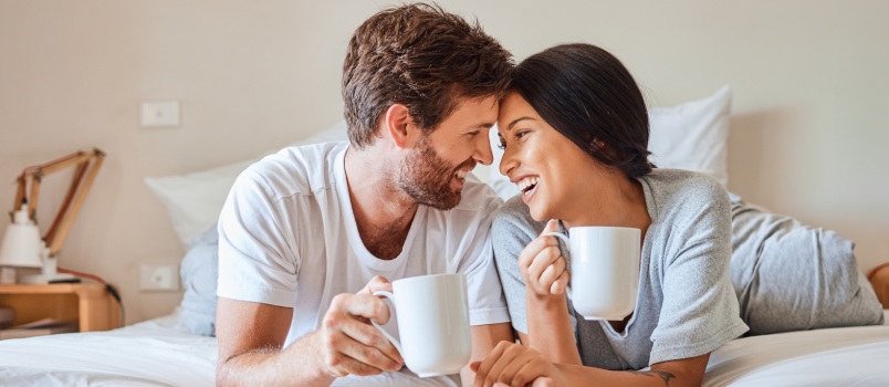 Happy couple drinking coffee in bedroom