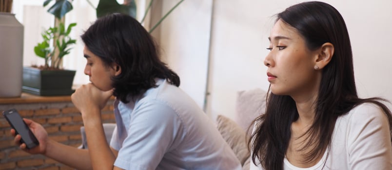 Wife looking at her husband while is using smartphone