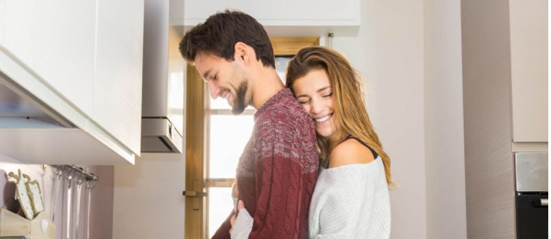 Happy women hugging husband while he is working in kitchen 