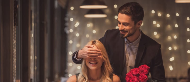 Handsome man holding flowers and covering women eyes