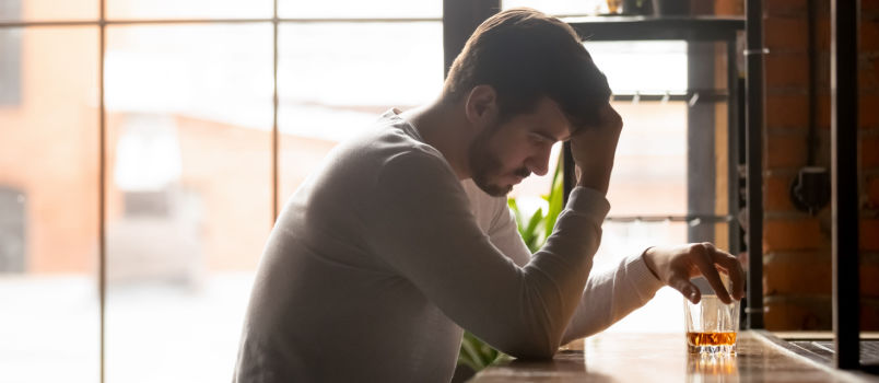 Depressed man sitting alone in bar having drink