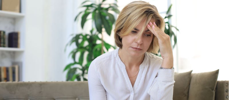 Unhappy middle aged woman sitting on couch