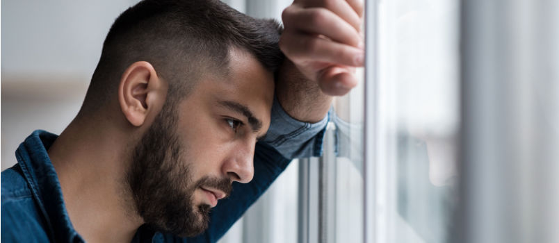 Sad man leaning forehead on window