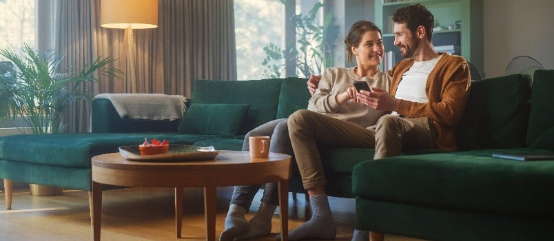 Happy couple sitting on couch using smartphone