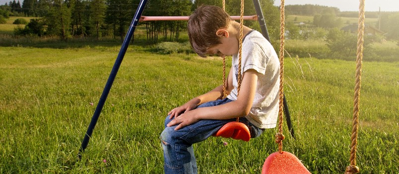 Sad boy sitting lonely on swing