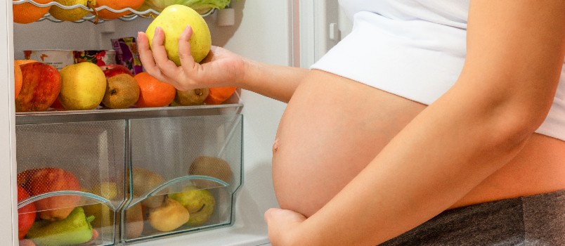 Woman holding orange standing near fridge