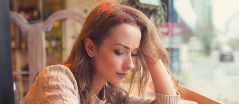 Young sad woman sitting alone on table 