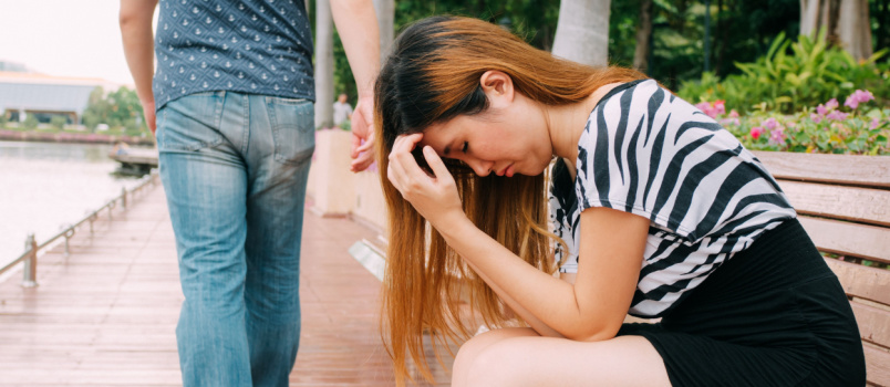 Sad woman siting on bench while man walking away