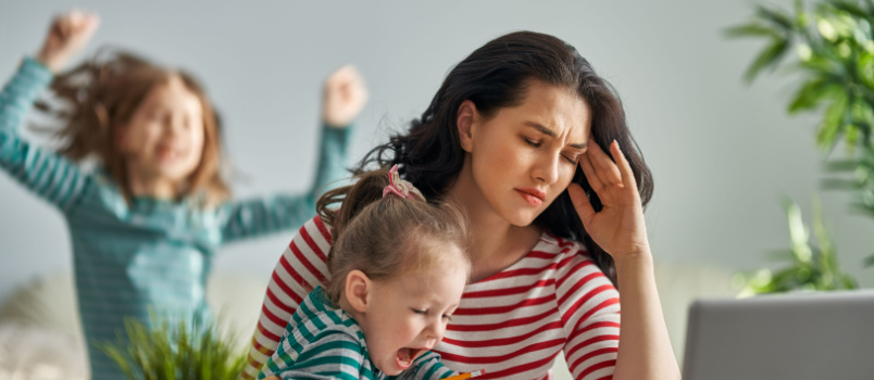 Woman working on laptop while handling kids