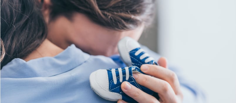 Woman hugging man while she is holding baby shoes