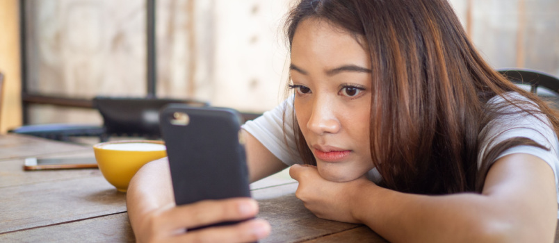 Sad woman laying on bed using smartphone