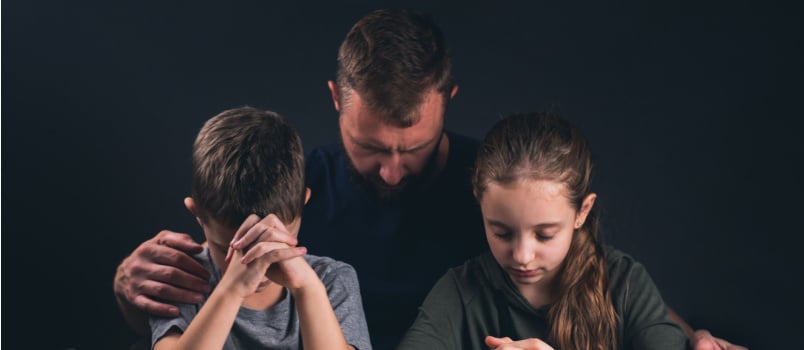 Dad and children praying open bible