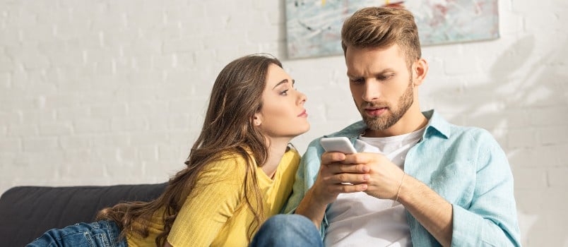 Attractive girlfriend looking at her boyfriend being busy in using smartphone
