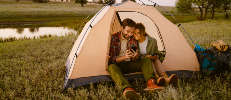 Couple using cellphone sitting in tent