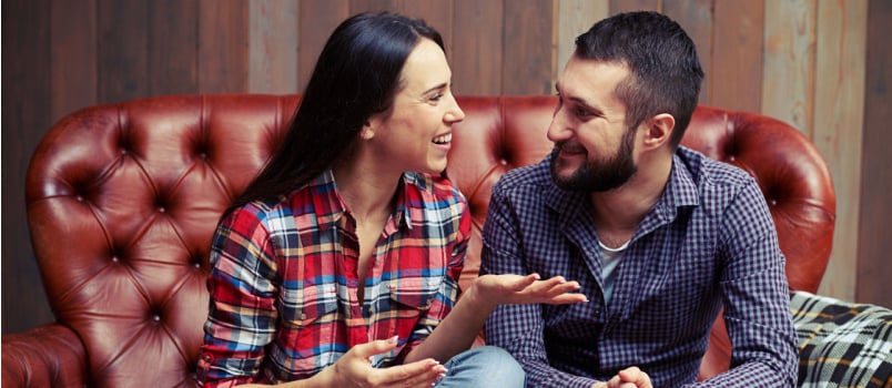 Happy couple sitting on couch talking to each other