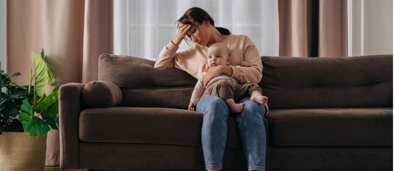 Depressed mother holding baby sitting on couch