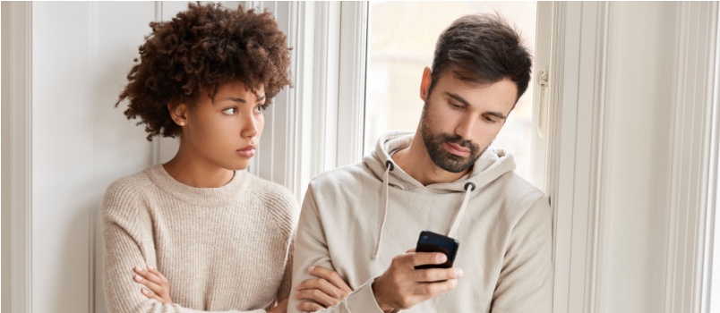 Jealous woman looking at man using smartphone