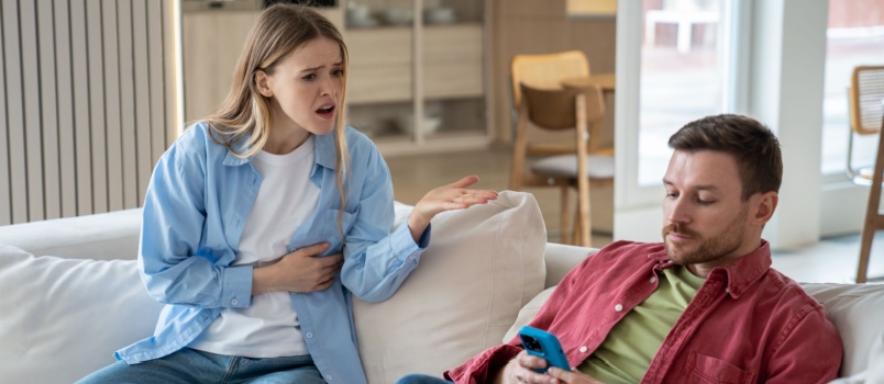 Wife getting irritated as husband is using phone while sitting with her