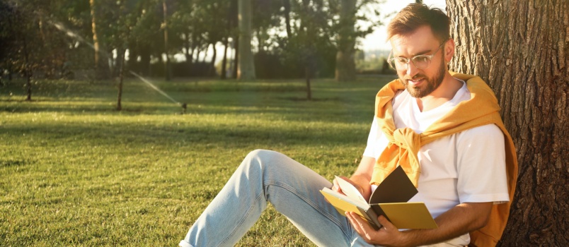 Young man reading book siting under the tree