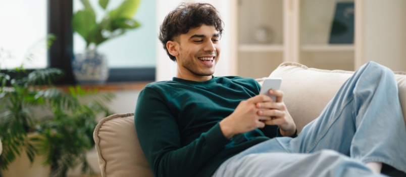 Young man sitting on couch using smartphone