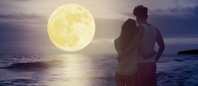 Couple standing on beach watching moon