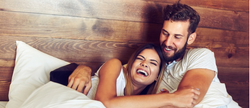 Young couple laying on bed laughing together