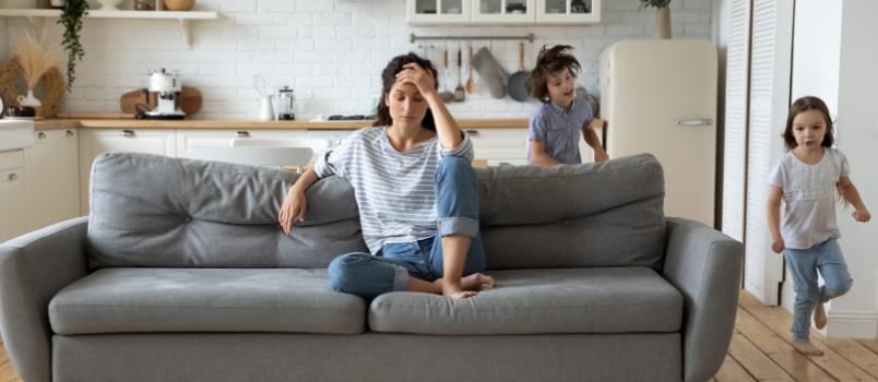 Young woman sitting on couch while kids are playing