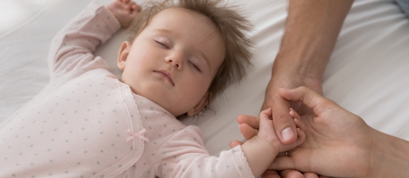 Baby holding parents hand while sleeping