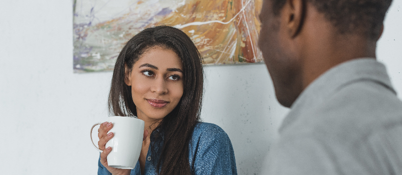 Woman Smiling at Man Drinking Coffee Indoors