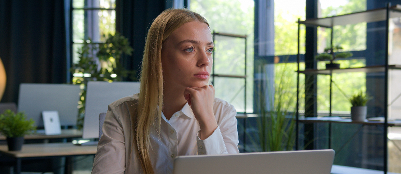 Woman Thinking At Desk With Laptop At Work