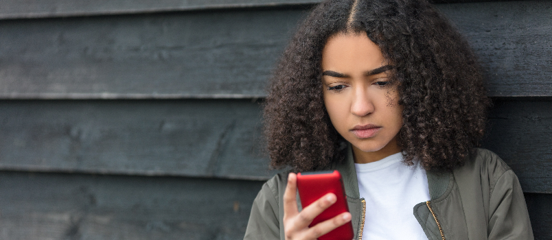 Une adolescente lit son téléphone, appuyée contre un mur
