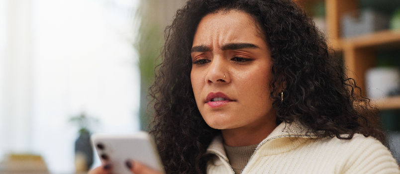 Concerned Young Woman Looking at Smartphone Screen Indoors
