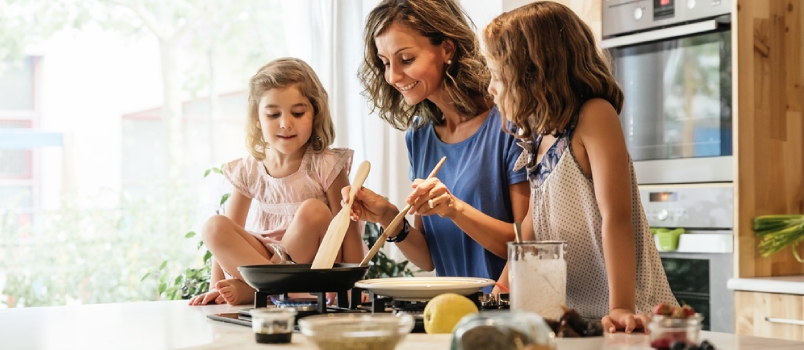 Mother Cooking In The Kitchen And Two Little Girls Watching